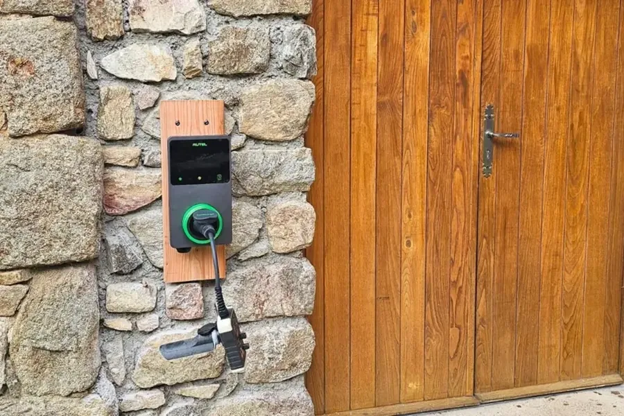 Borne de recharge murale posée sur un mur en pierre, à côté d’une porte en bois